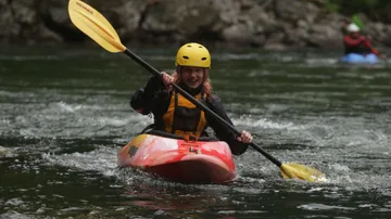 Person kayaking on a river wearing helmet.