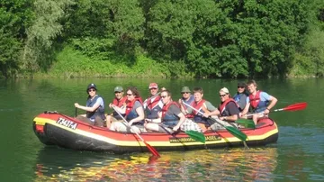 Gruppe paddelt auf Floß im Fluss, umgeben von Bäumen.