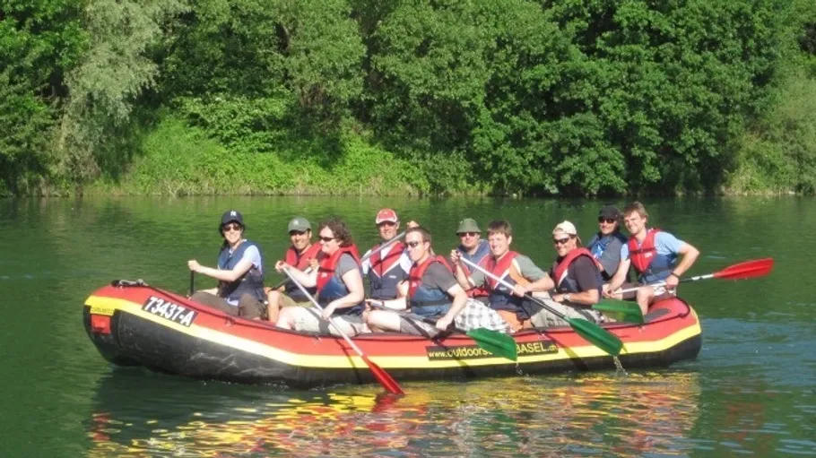 Gruppe paddelt auf Floß im Fluss, umgeben von Bäumen.