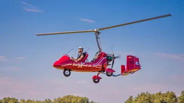 Red helicopter flying over a forest area.