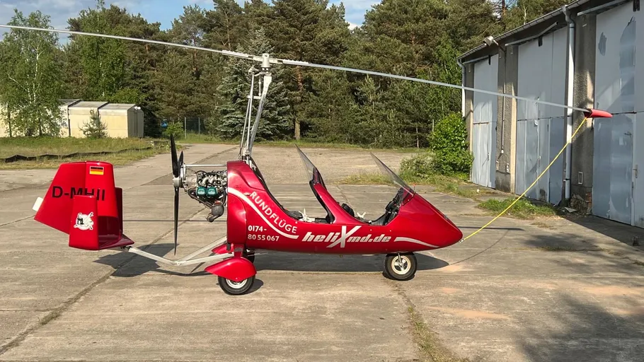 Red gyrocopter parked on concrete airfield.