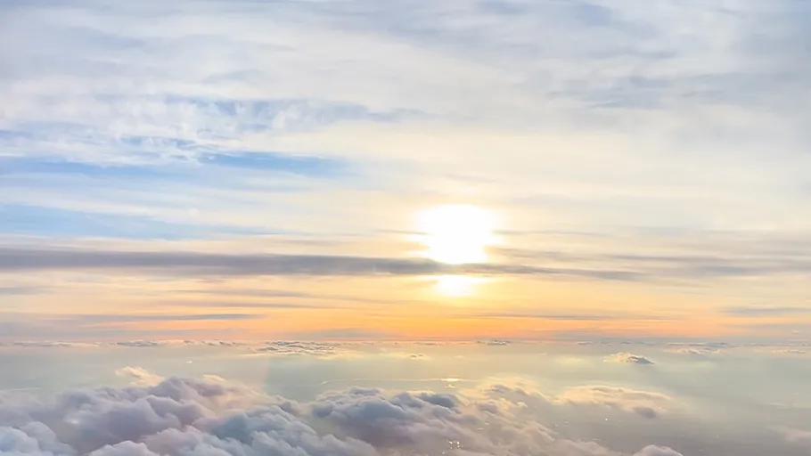 Sun setting over fluffy clouds, sky view.