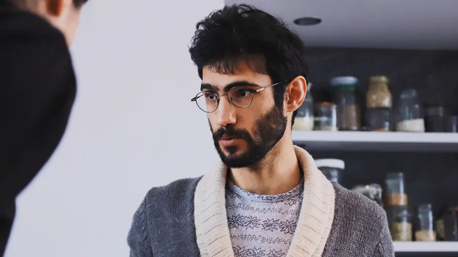 Bearded man with glasses listens in kitchen.
