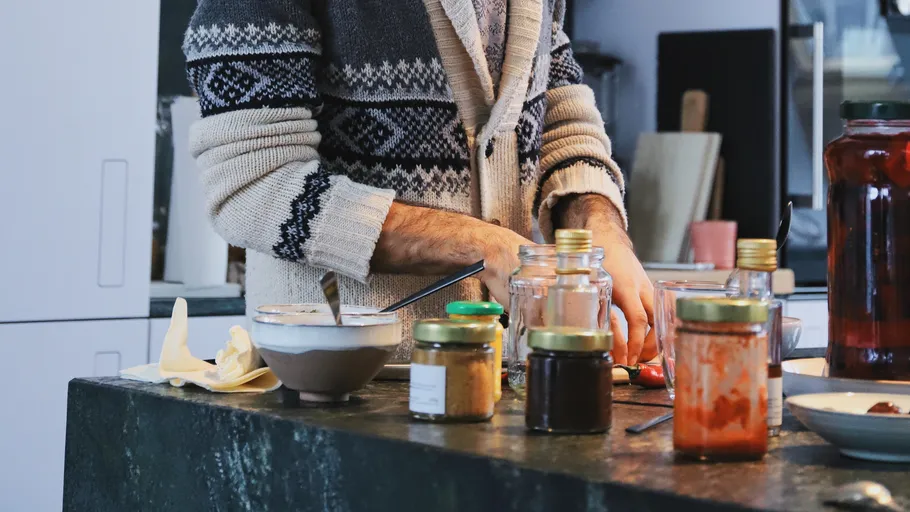 Person cooking with jars on the kitchen counter.