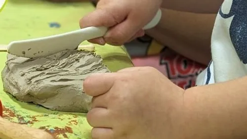 Child molding clay with plastic tool.