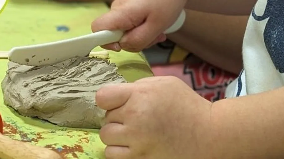 Child molding clay with plastic tool.