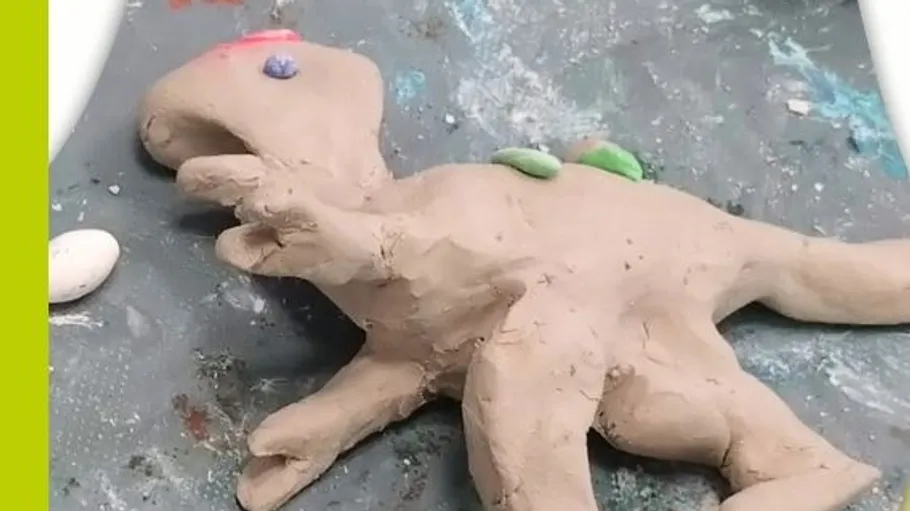 Ton-Dinosaurier-Skulptur auf unordentlicher Oberfläche.
