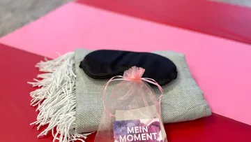 Eye mask on blanket, pink gift bag nearby.