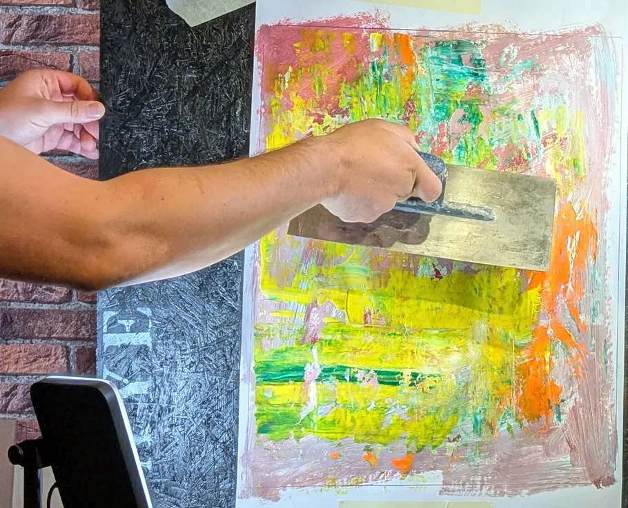 Person using trowel on colorful painting surface.