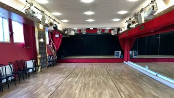 Empty dance studio with wooden floor, mirrors, chairs.