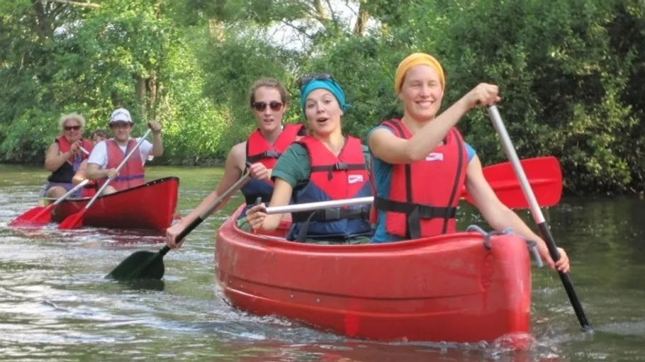 Group paddling red canoes on a river.