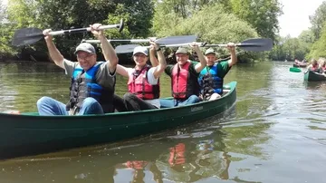 Vier Personen paddeln in einem Kanu auf Fluss.