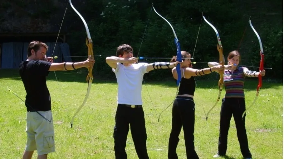 Four people aiming bows outdoors.