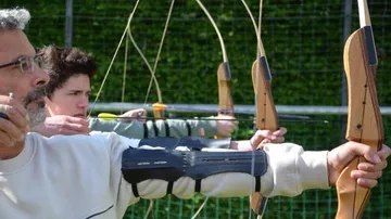 People aiming bows at outdoor archery range.