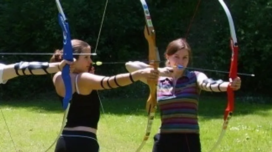 Women shooting arrows in sunny outdoor setting.