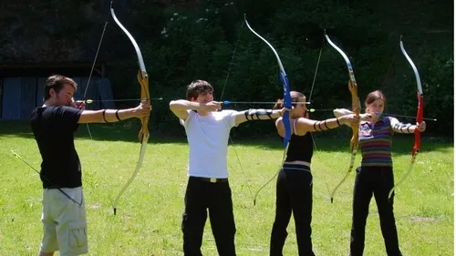 Four people aiming bows in a grassy field.