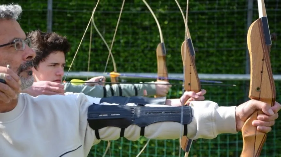 Archers aiming bows outdoors in a line.