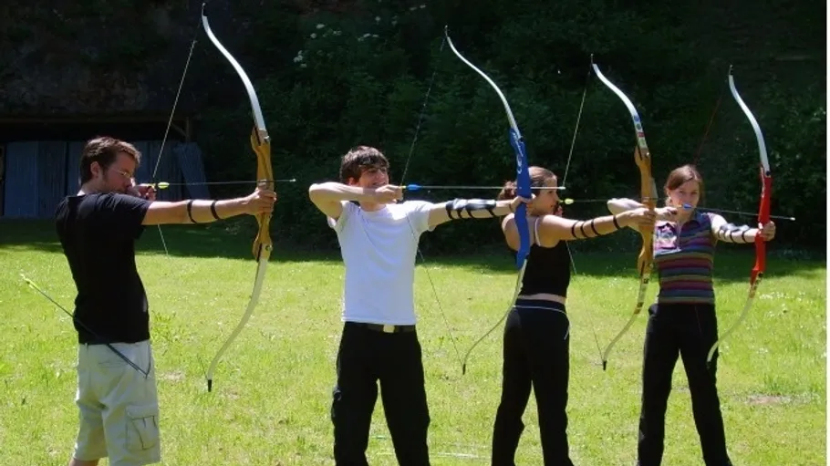 Four people aiming bows in a field.