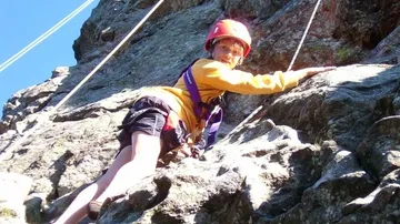 Climber in helmet scaling rocky cliff.