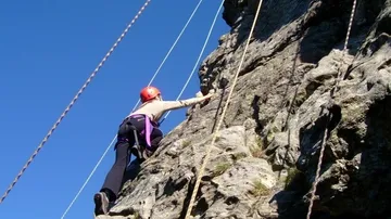 Kletterer steigt Felswand mit Sicherheitsseilen hinauf.
