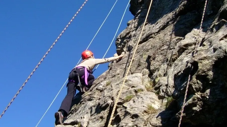 Climber ascending rock wall with safety ropes.
