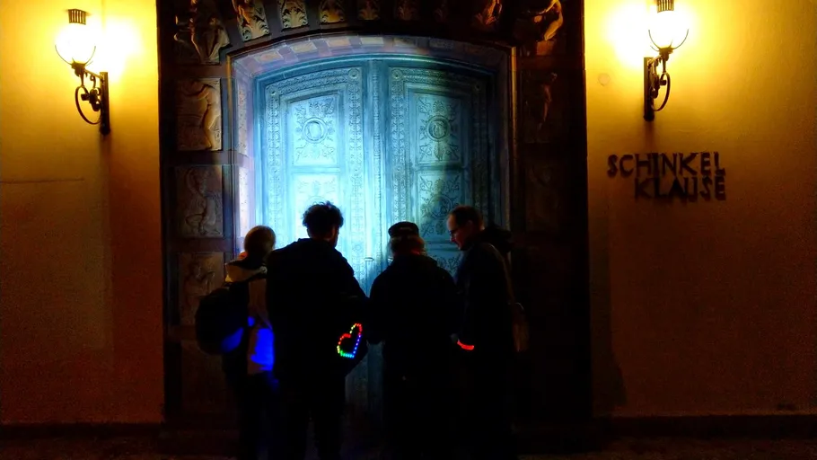 People with glowing bags stand at ornate door.