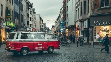 Red van driving through busy city street.