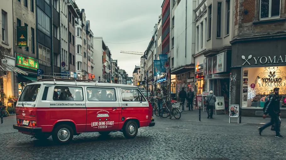Roter Van fährt durch belebte Stadtstraße.