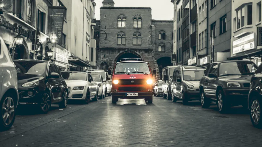 Red van driving on narrow city street.