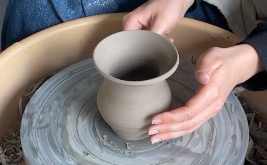 Hands shaping pottery on a spinning wheel.