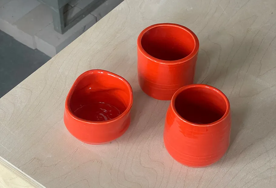 Three red ceramic cups on wooden surface.