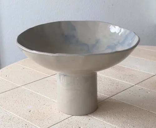 Keramikschale auf Sockel auf gekacheltem Tisch.