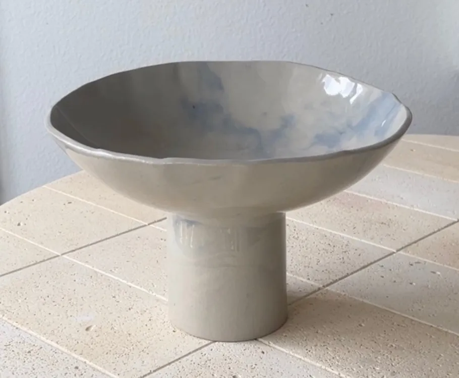 Keramikschale auf Sockel auf gekacheltem Tisch.