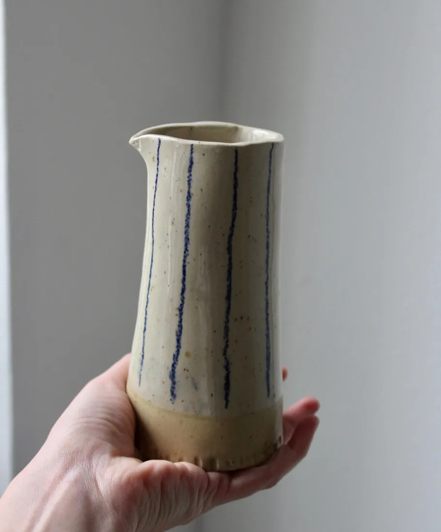 Hand holds ceramic jug with vertical blue stripes.