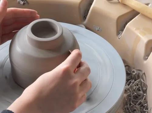 Hands shaping clay bowl on pottery wheel.