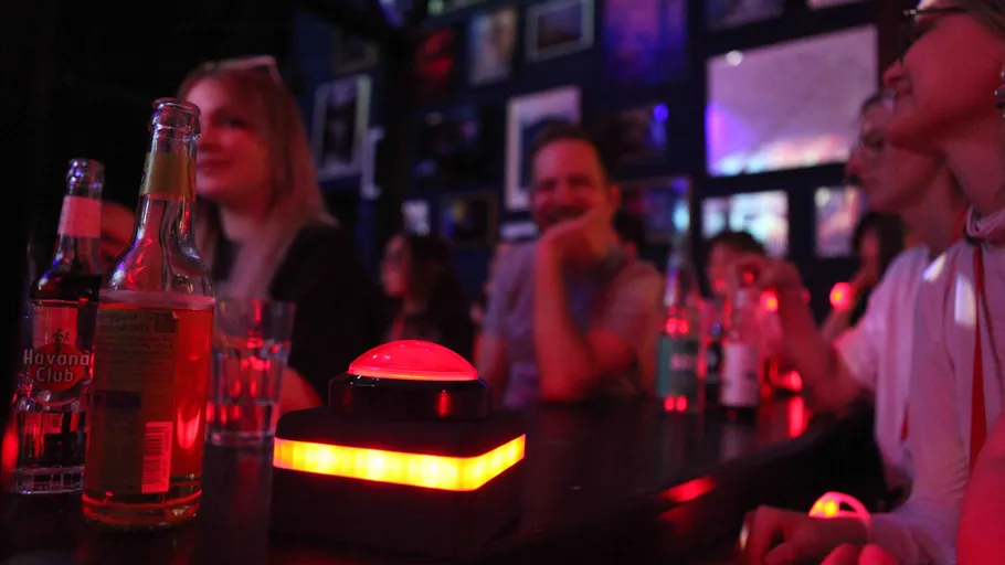 Menschen sitzen mit Getränken und einem Buzzer.