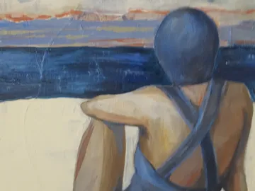 A person is sitting on the beach and looking at the water.
