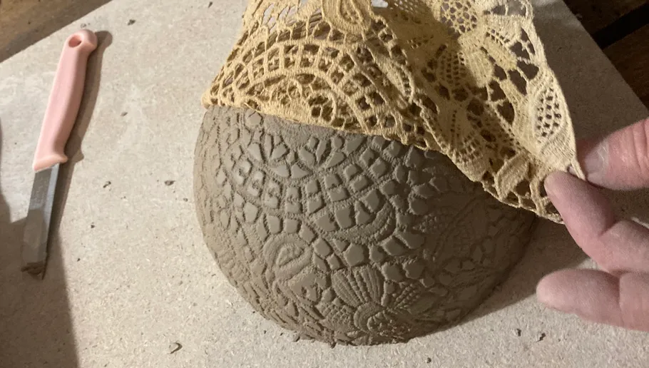 Clay bowl textured with lace pattern, hand visible.
