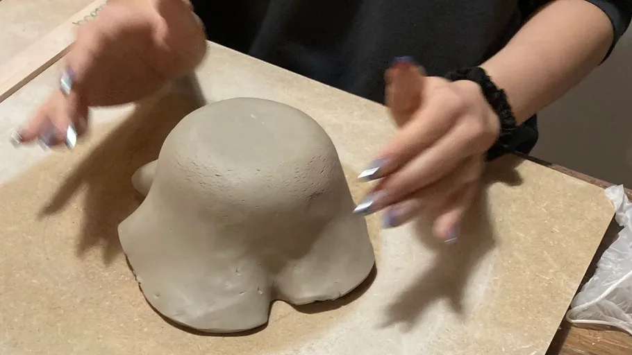 Hands shaping clay on a table.