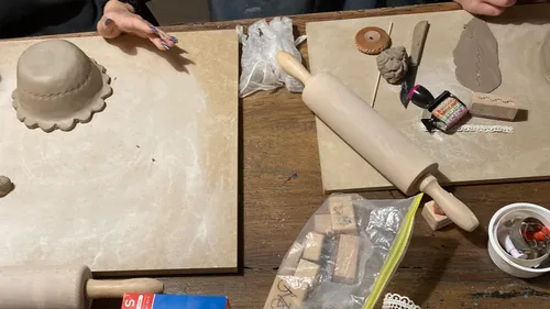 Hände formen Ton auf Tisch mit Werkzeugen.