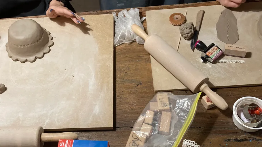 Hände formen Ton auf Tisch mit Werkzeugen.