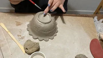 Hände formen eine Tonschale auf einem Tisch.