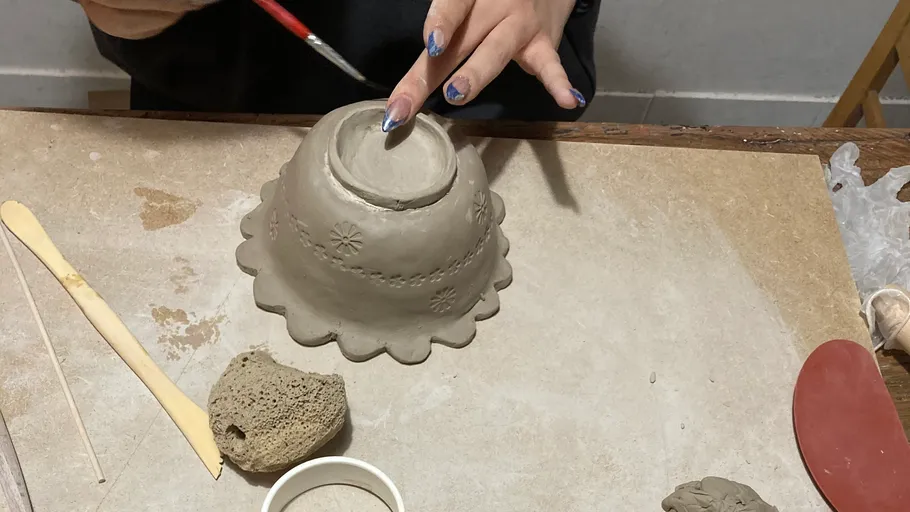 Hände formen eine Tonschale auf einem Tisch.