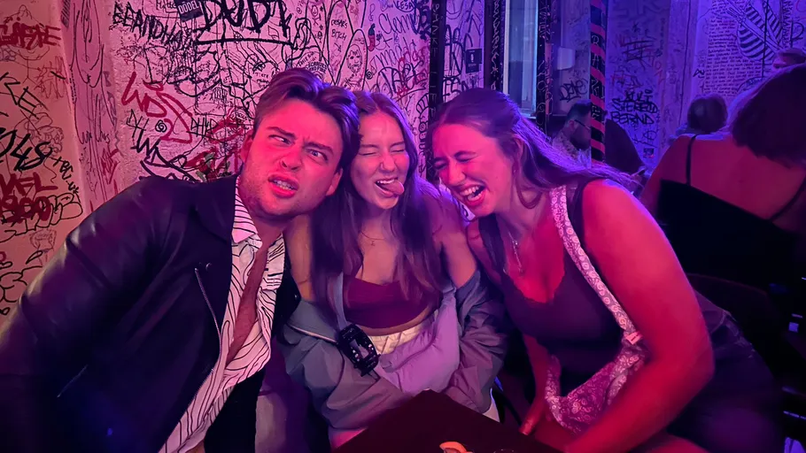 Three people making funny faces in graffiti-covered room.
