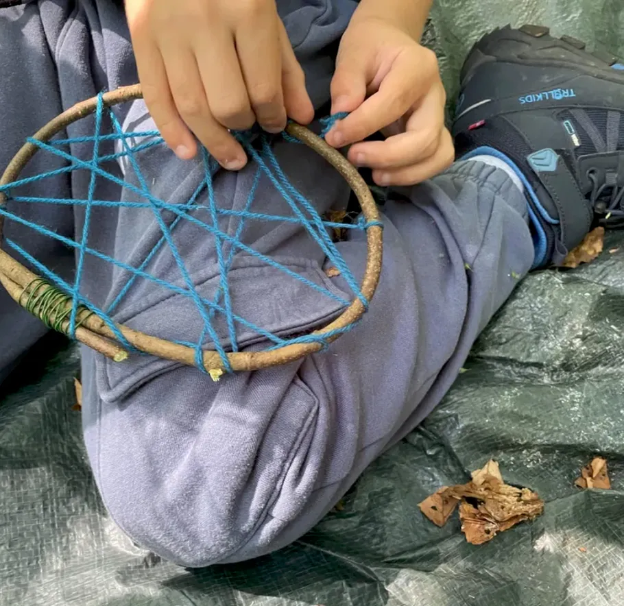 Kind fädelt blaue Schnur auf Holzreifen.