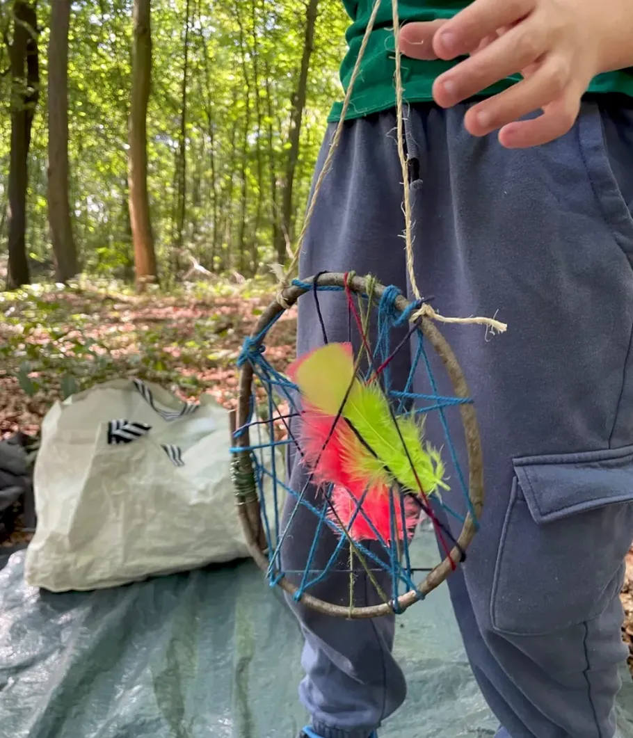Child holding handmade dreamcatcher in forest.