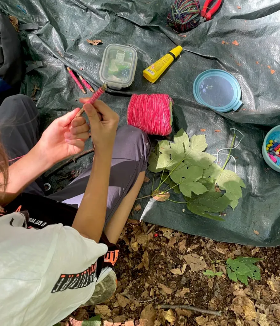 Person crafting on a tarp with yarn and leaves.