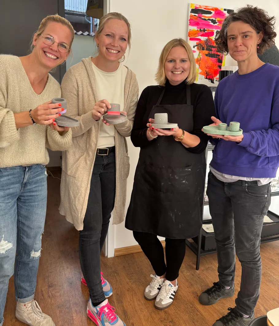 Four people hold handmade ceramics indoors.