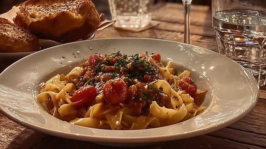 Pasta dish with bread on wooden table.