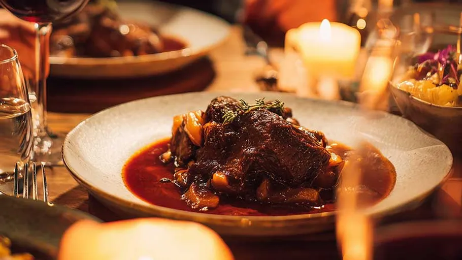 Plate of braised meat with sauce, dimly lit table.
